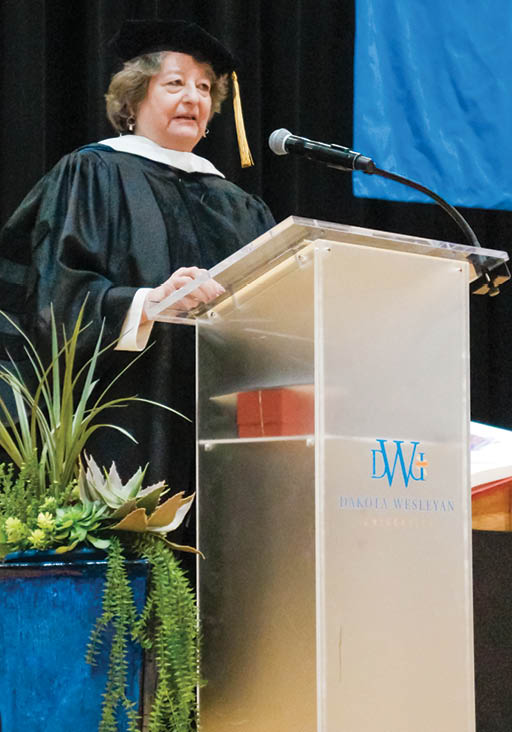 A woman in a black robe stands at a podium. Description generated by AI