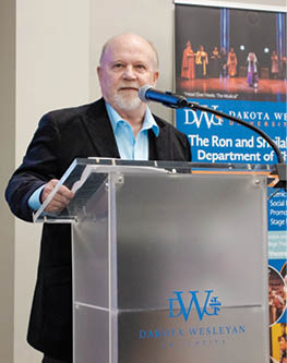 A man giving a speech in front of a podium. Description generated by AI